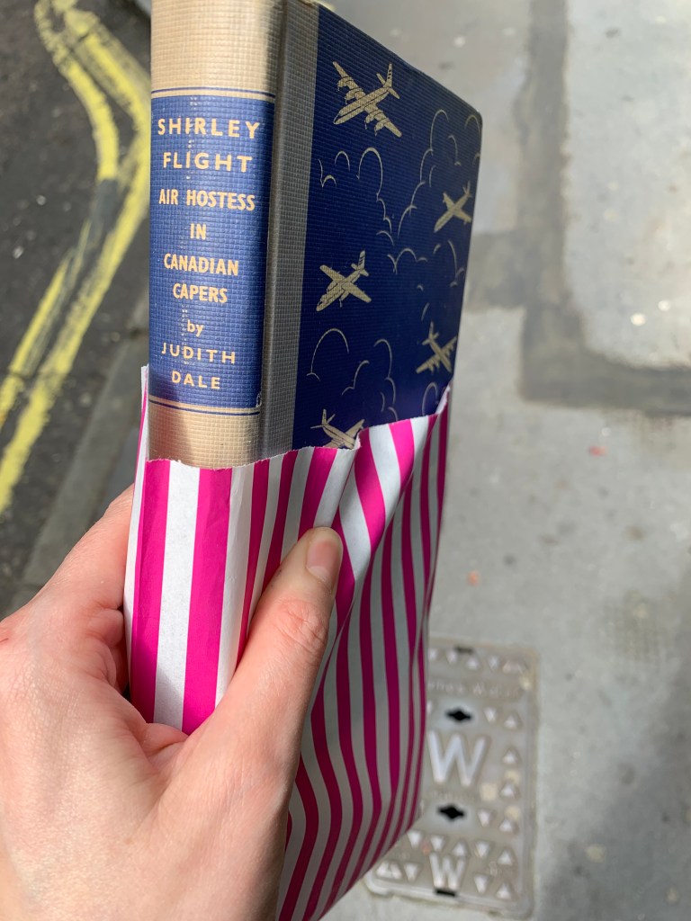 Copy of Shirley Flight Air Hostess in Canadian Capers in a pink and white striped paper bag.