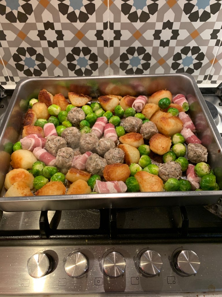 A large tin full of roast potatoes, brussel sprouts, stuffing balls and pigs in blankets