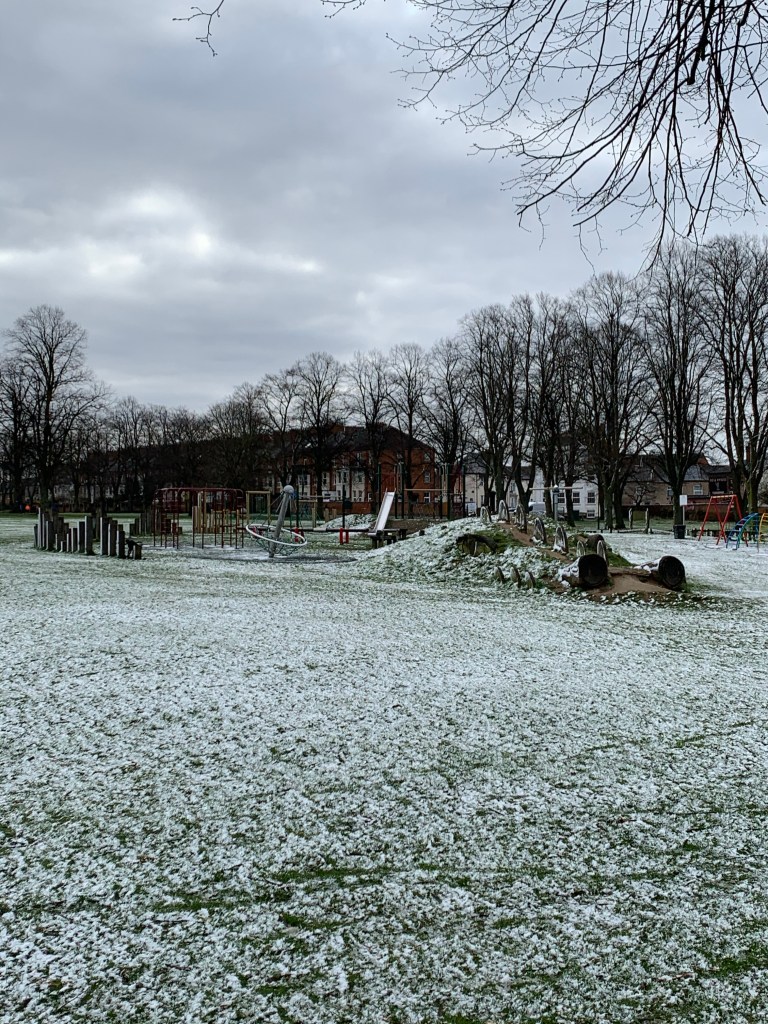 Snowy grass and play equipment under a heavy grey sky